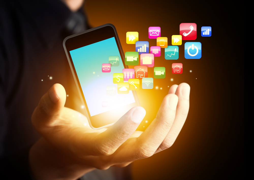 Close up of a man's handing holding a cell phone with the apps floating off the screen of the phone.