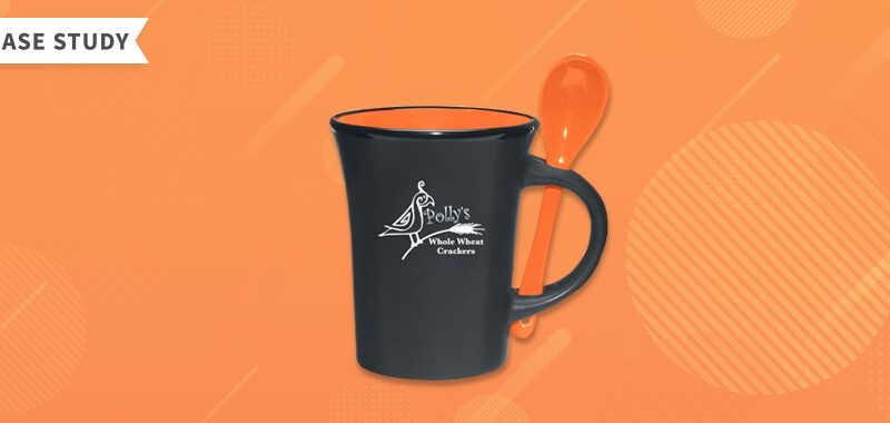 Black ceramic mug with orange spoon attached and Polly's Whole Wheat Crackers logo on the front.