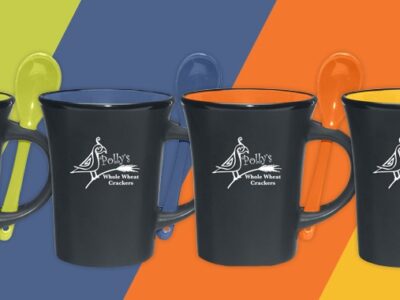Four black ceramic mugs, each having a different color on the inside of green, blue, orange and yellow with Polly's Whole Wheat Crackers logo on the front.